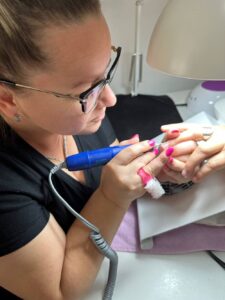 Student na slici radi aparatni manikir frezom na baznoj obuci za nokte.